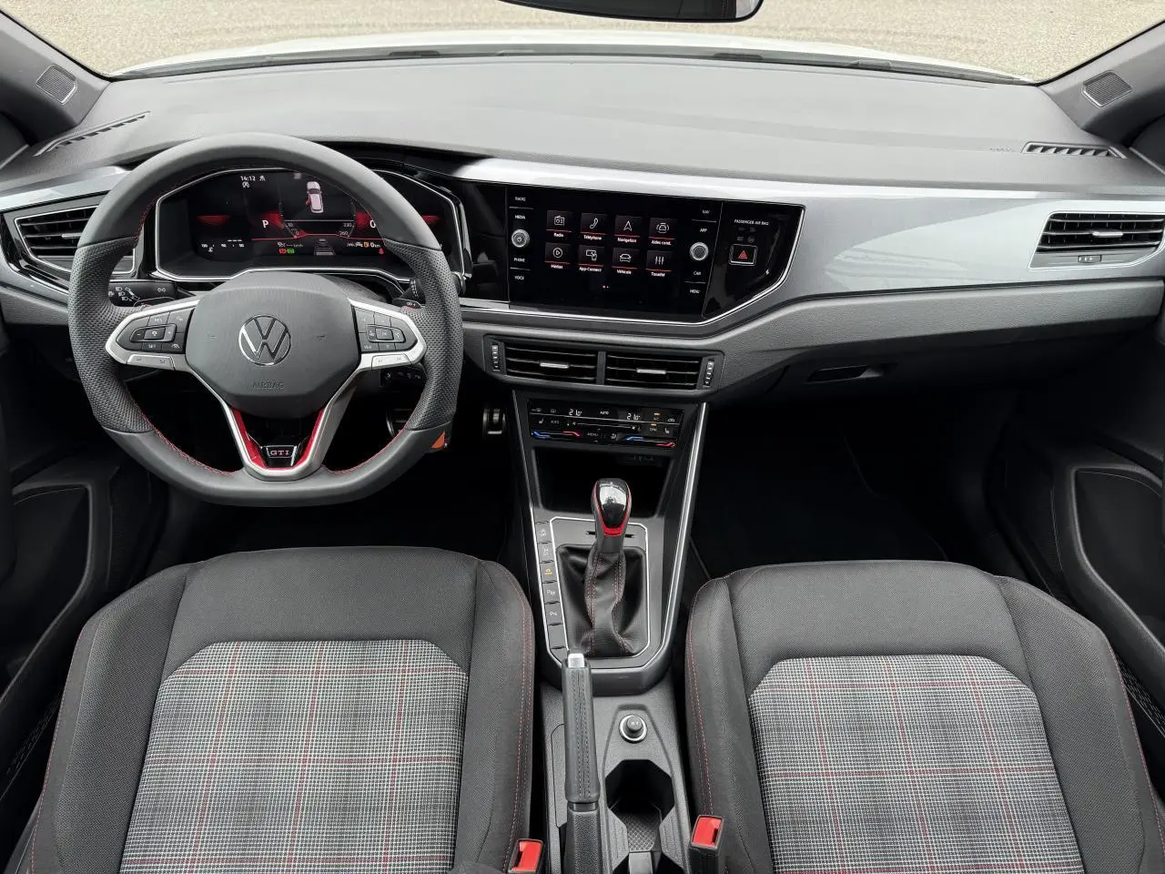 Vue intérieure avant de la Volkswagen Polo GTI 2024, tableau de bord moderne avec volant sport et sièges à motif tartan.