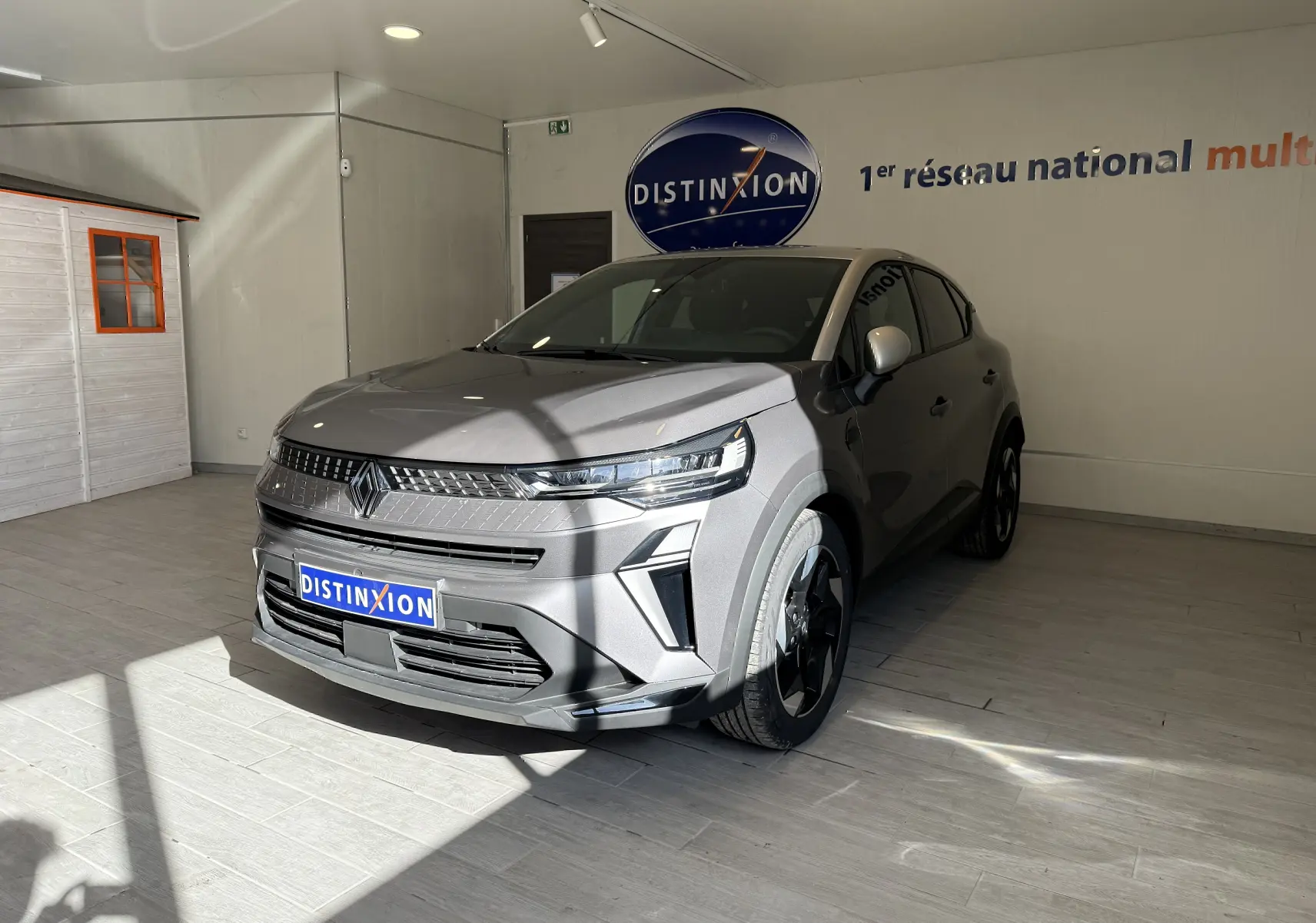 Renault Captur 2025 gris Cassiopée métal avec toit gris, vue 3/4 avant en intérieur lumineux showroom Distinxion.