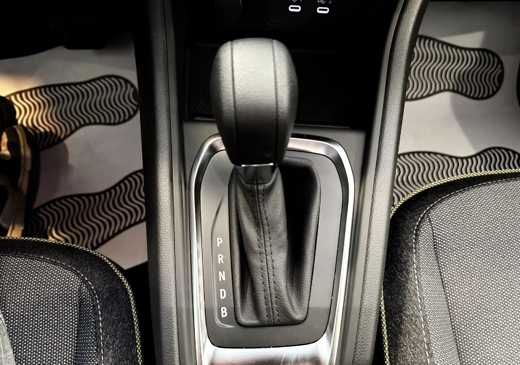 Le levier de vitesses automatique noir du Renault Captur 1.6 E-TECH en gros plan, entouré de sièges gris à surpiqûres jaunes.