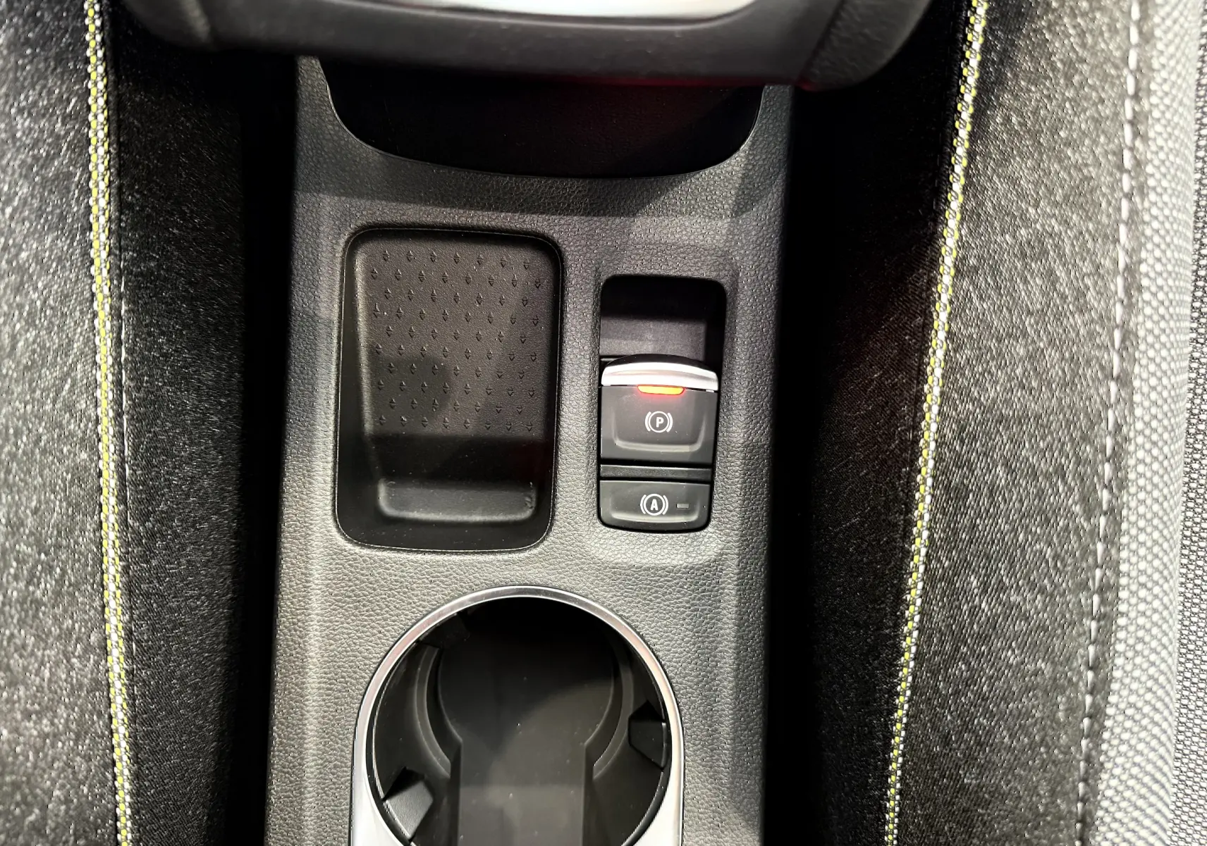 Gros plan sur la console centrale du Renault Captur gris, montrant le frein à main électrique et les surpiqûres jaunes des sièges.