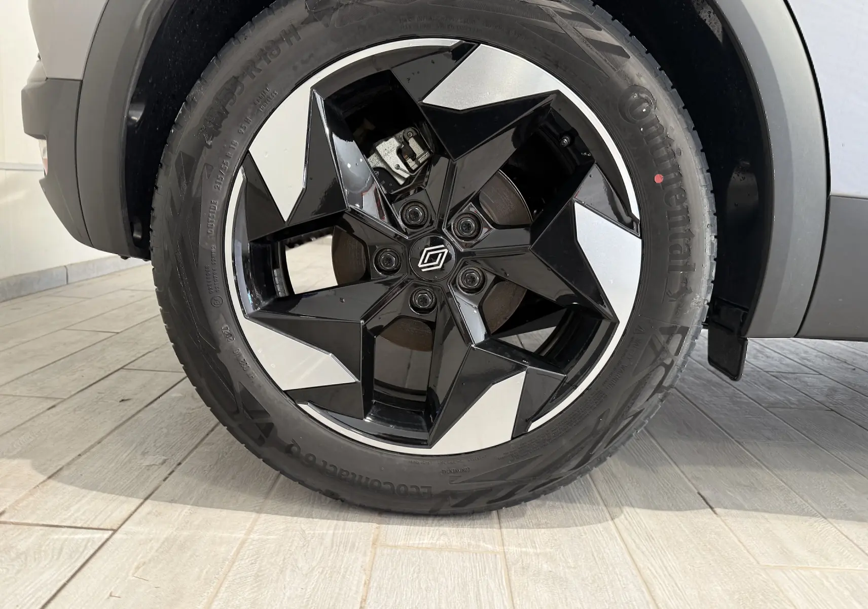Gros plan sur la roue avant droite du Renault Captur gris Cassiopée, mettant en valeur la jante noire et argentée au design étoilé.