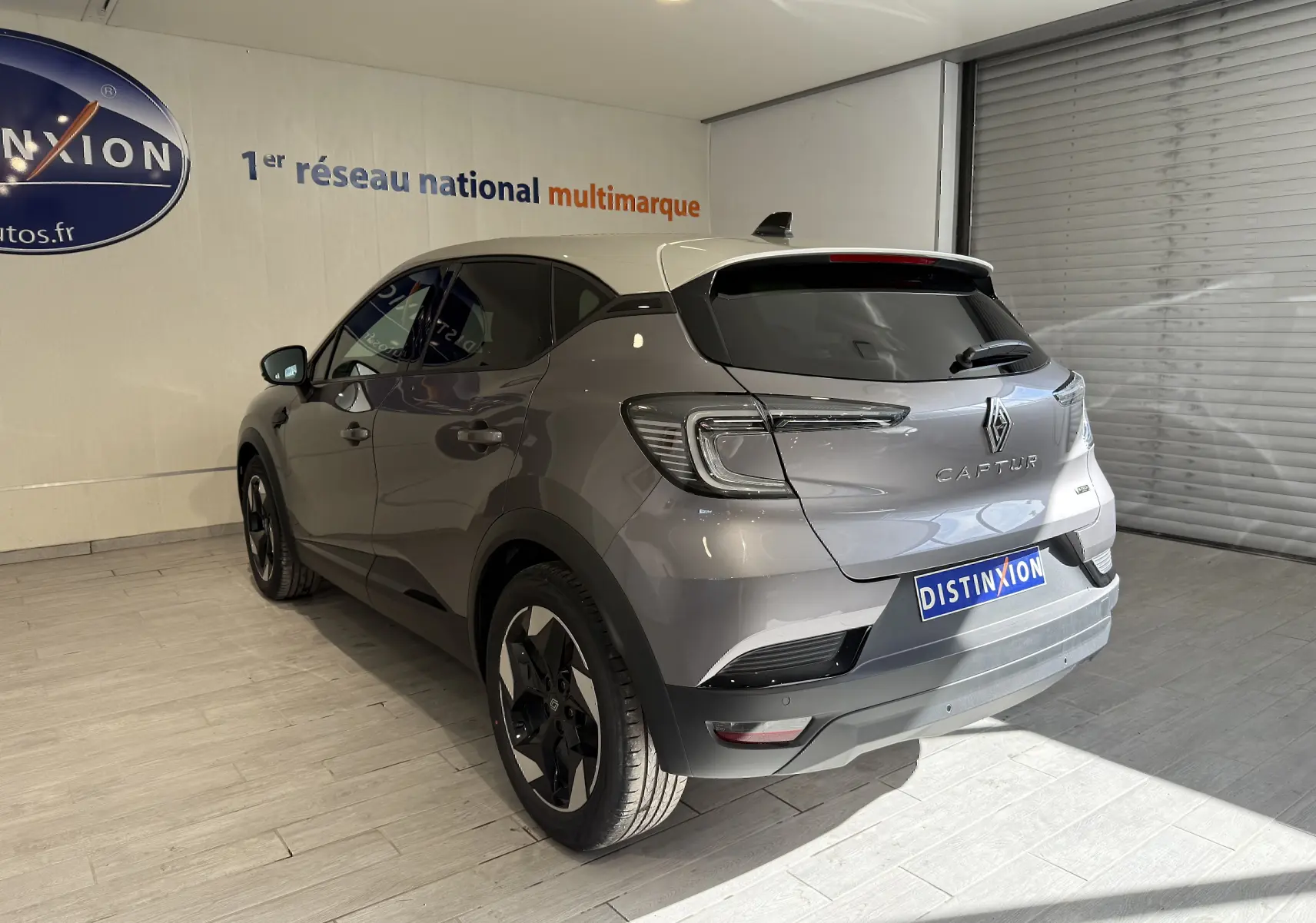 Vue 3/4 arrière droite du Renault Captur gris Cassiopée métal avec toit gris, en intérieur showroom lumineux.