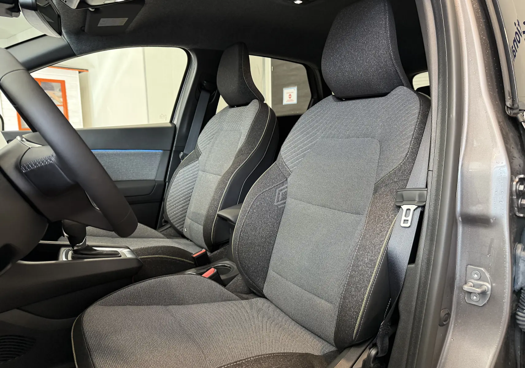Vue intérieure côté gauche des sièges avant gris du Renault Captur 2025 hybride avec portière ouverte.