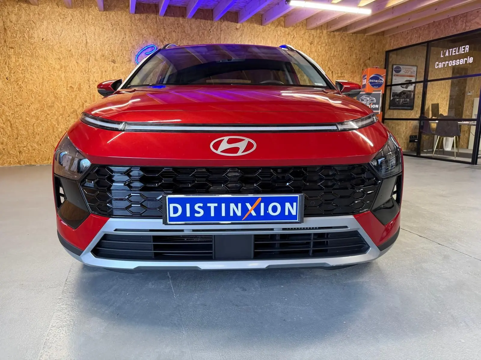 Vue frontale d'un Hyundai Bayon rouge avec calandre noir laqué et plaque Distinxion en intérieur d'atelier.