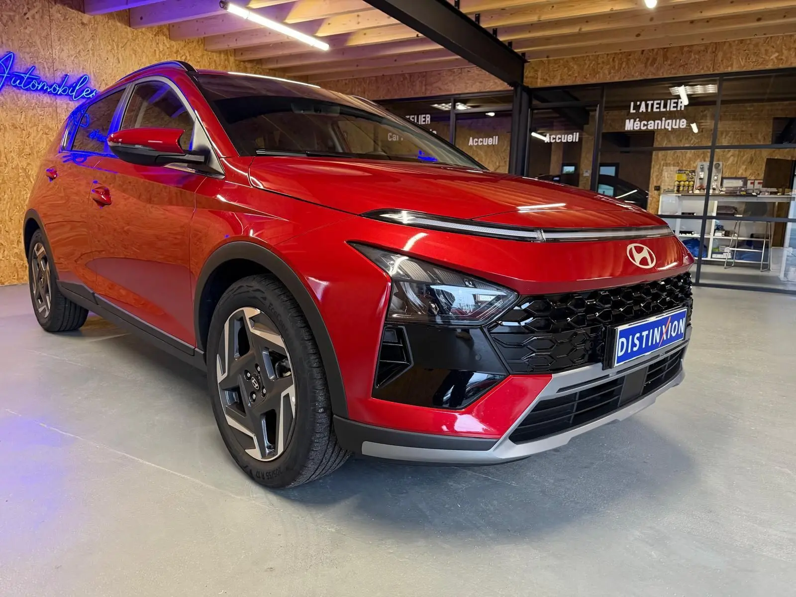 Vue 3/4 avant gauche d'une Hyundai Bayon rouge avec calandre noir laqué et jantes alu 17 pouces en intérieur showroom.
