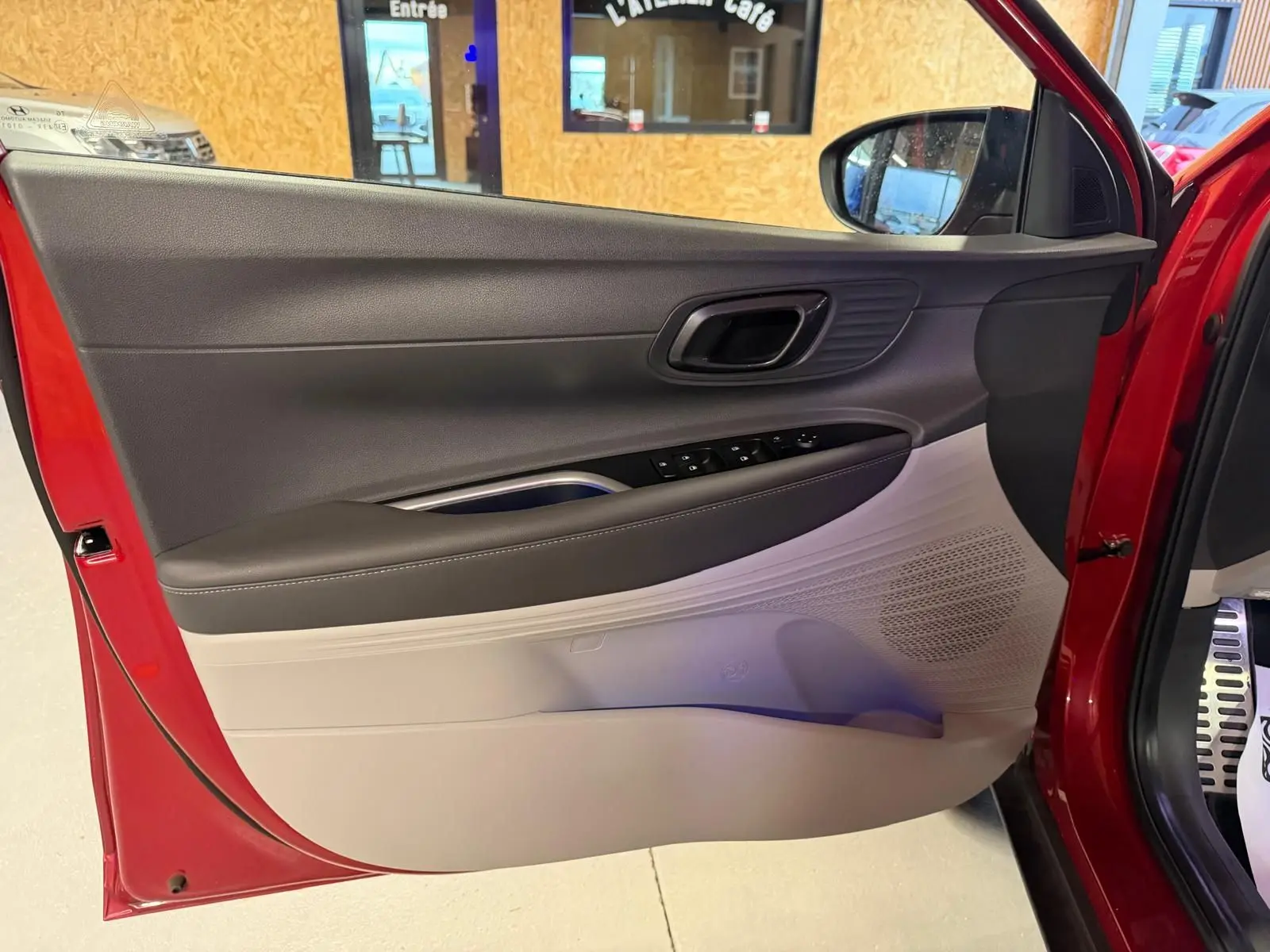 Porte avant gauche ouverte d'une Hyundai Bayon rouge 2025, intérieur bi-ton noir et gris clair avec commandes électriques.