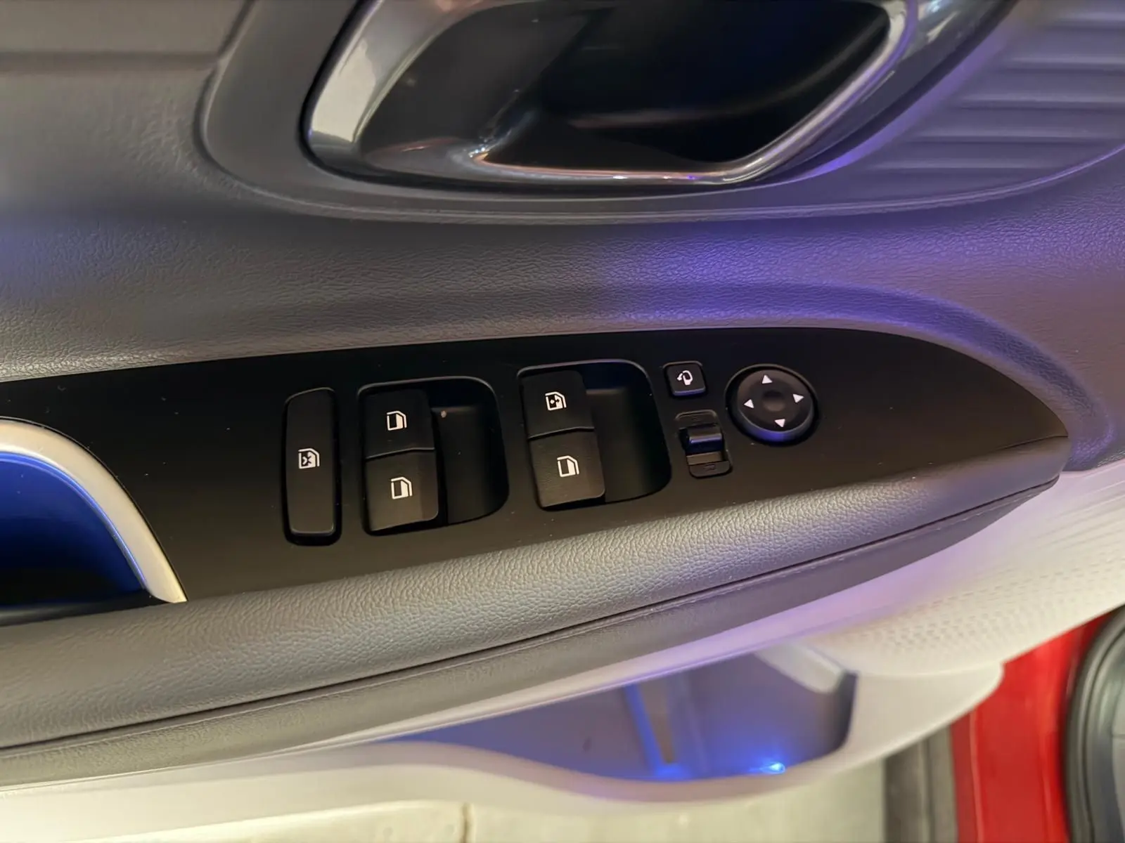 Gros plan sur les commandes de vitres et rétroviseurs côté gauche d'une Hyundai Bayon rouge avec éclairage d'ambiance bleu.