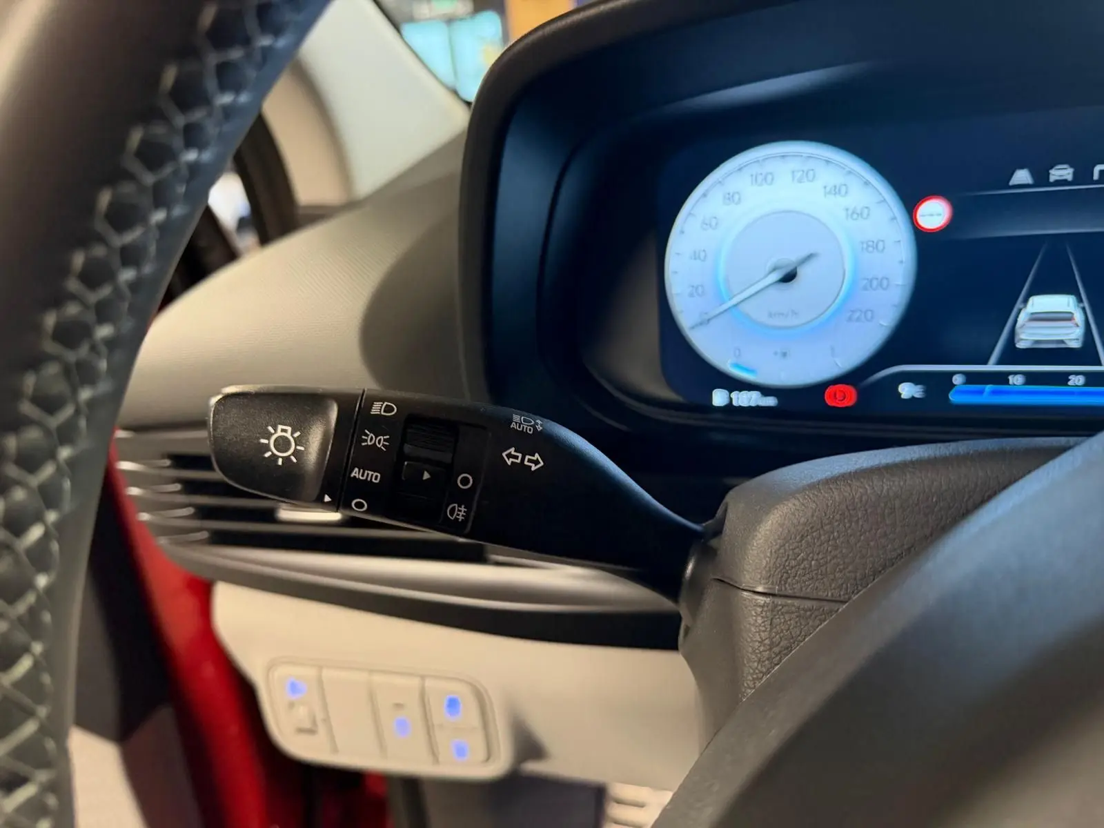 Gros plan sur la manette des feux et le tableau de bord numérique bleu d'une Hyundai Bayon rouge, côté gauche.