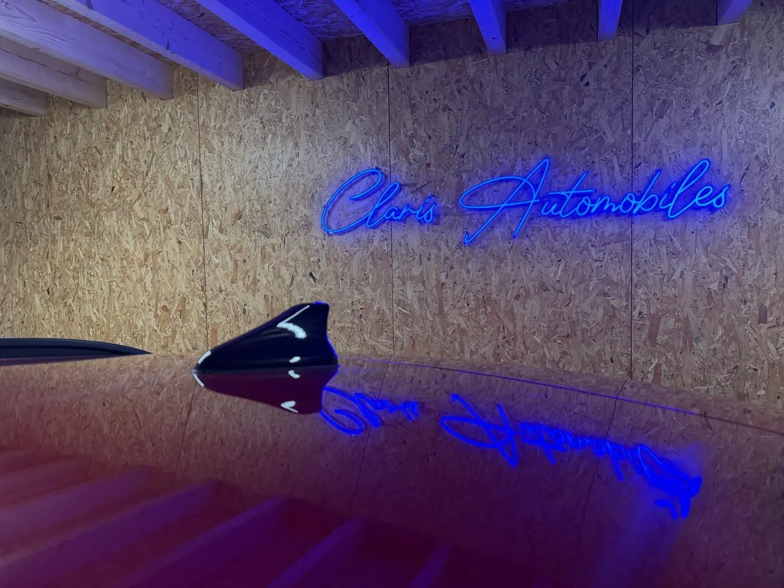 Antenne requin noire sur le toit d'une Hyundai Bayon rouge, reflet du néon bleu "Claris Automobiles" sur la carrosserie.