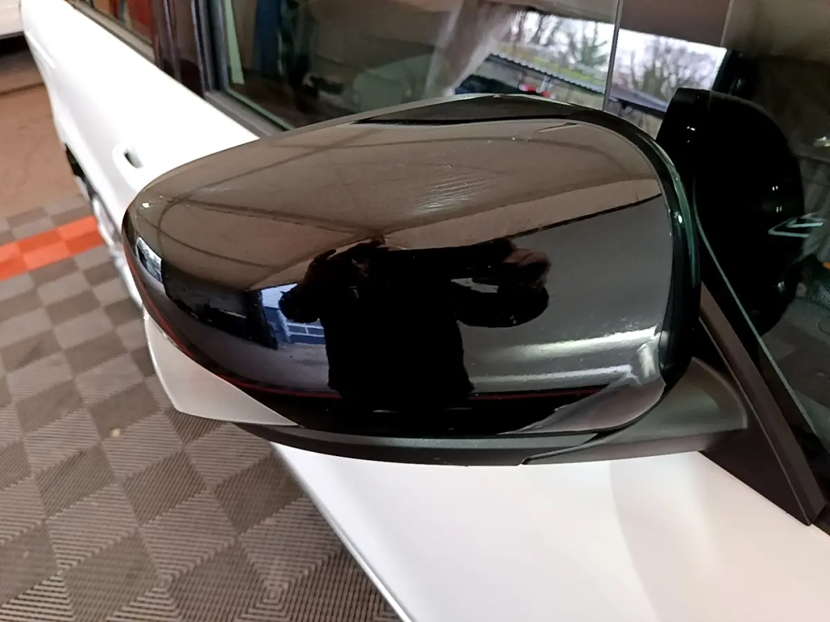 Rétroviseur noir en gros plan côté gauche d’un Renault Kangoo blanc, avec reflet intérieur visible.