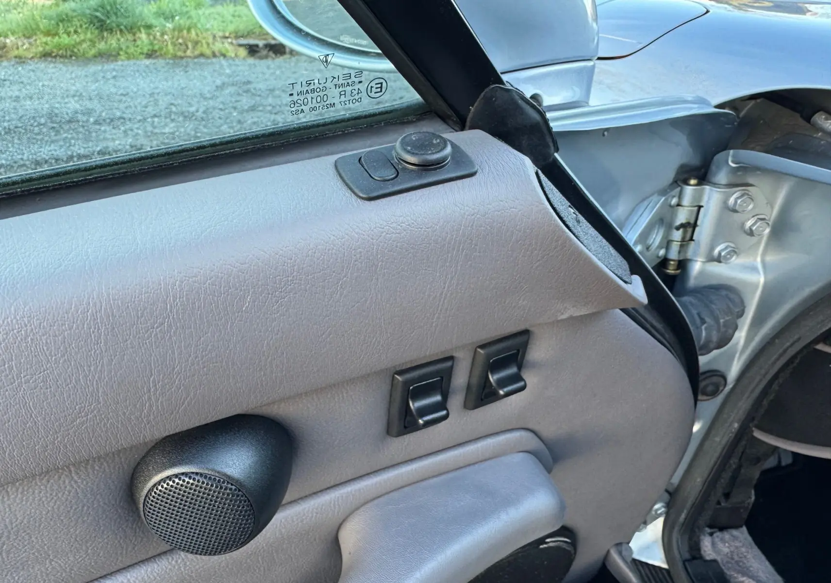 Détail de la porte côté conducteur gris clair d’une Porsche 911 Carrera 2 type 993 avec commandes de vitres électriques et haut-parleur.