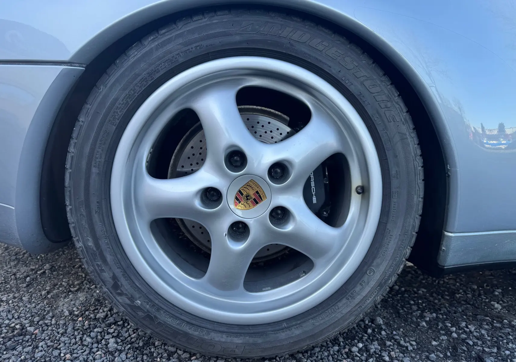 Gros plan sur la roue avant gauche gris polaire d'une Porsche 911 Carrera 993 avec jante alliage et logo Porsche central.