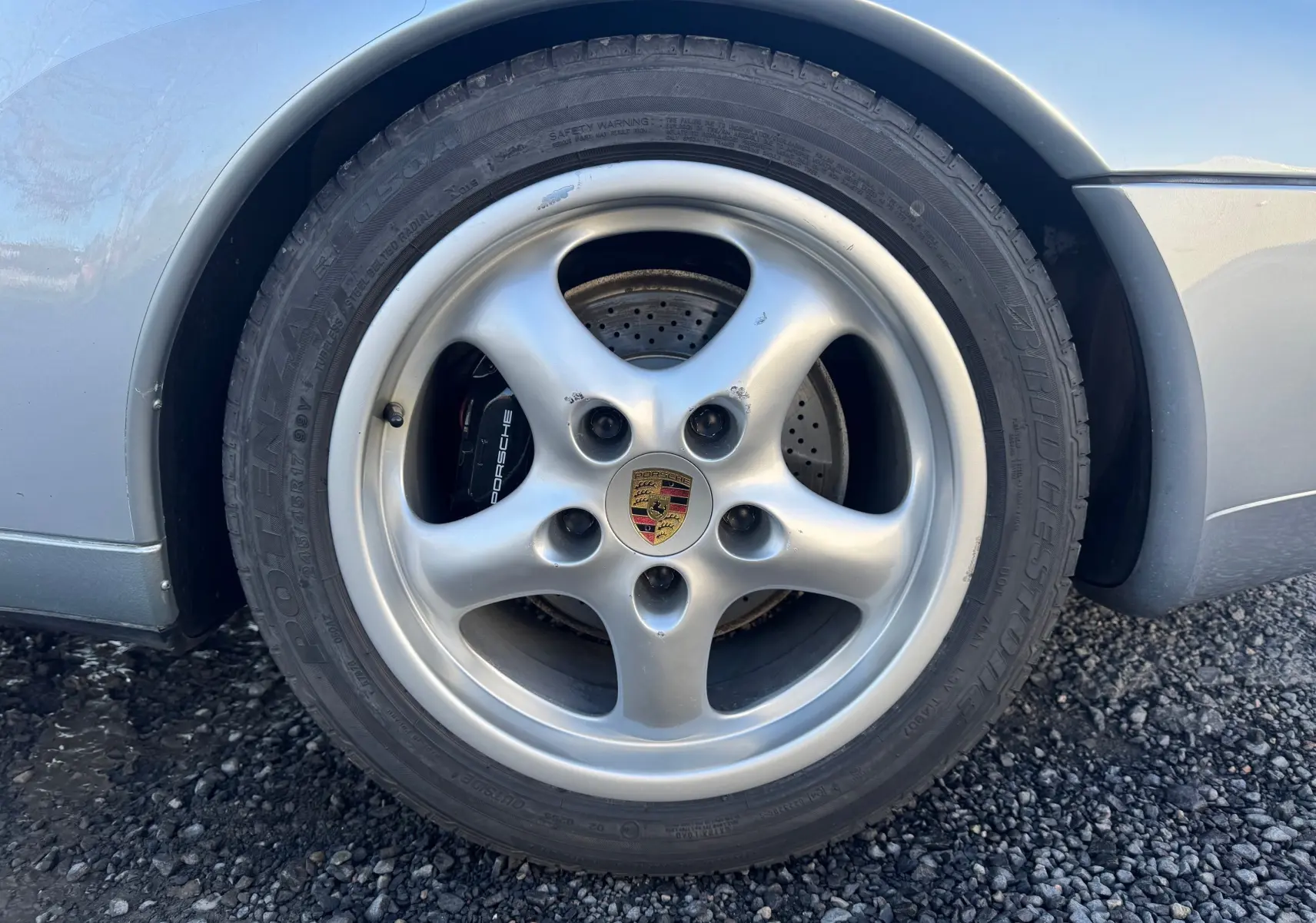 Gros plan sur la roue avant droite gris polaire d'une Porsche 911 Carrera 2 Type 993 avec jante 17 pouces et étrier Porsche visible.