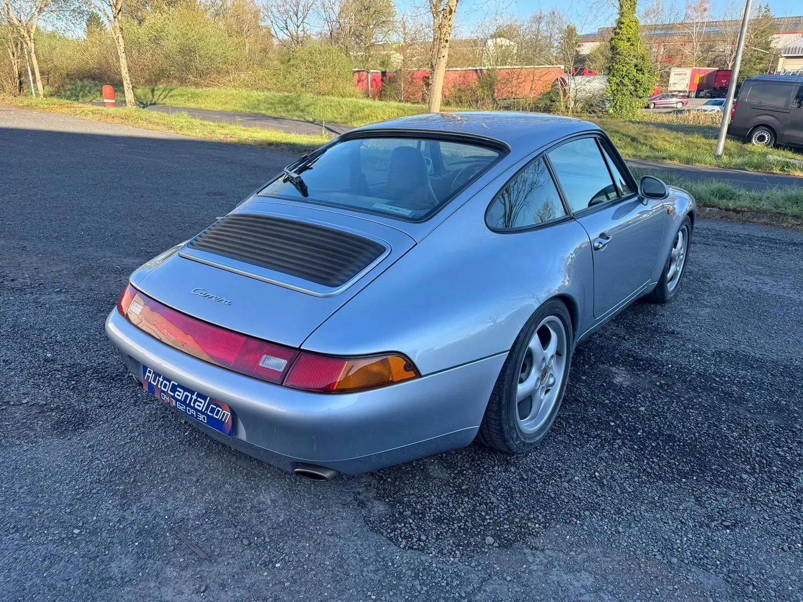 Vue 3/4 arrière droite d'une Porsche 911 Carrera 993 gris polaire avec jantes 17 pouces et pare-brise teinté dégradé.