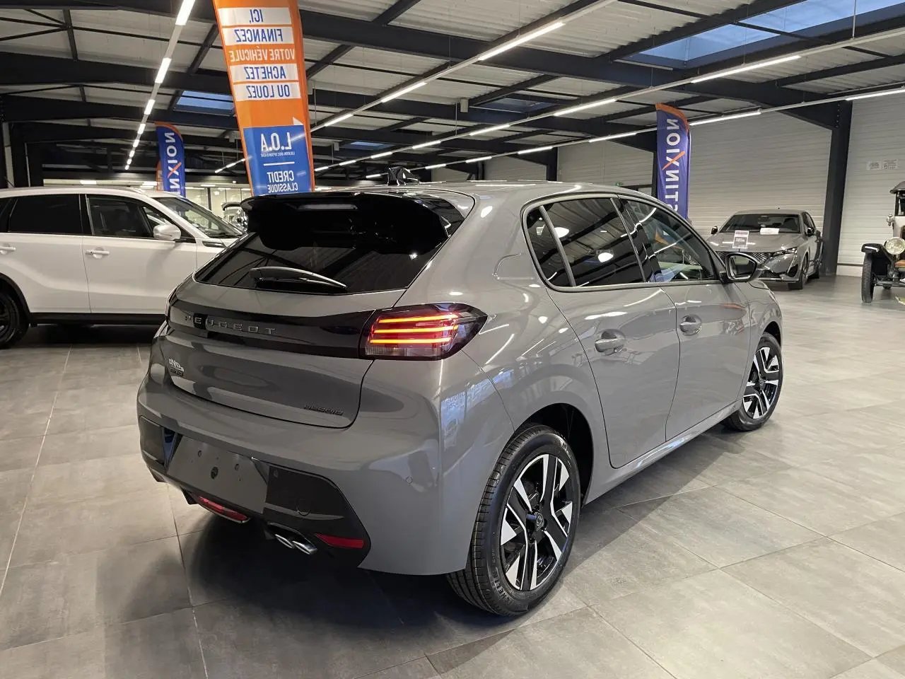 Peugeot 208 gris Selenium vue 3/4 arrière droit en intérieur avec jantes alliage bi-tons et feux LED allumés.