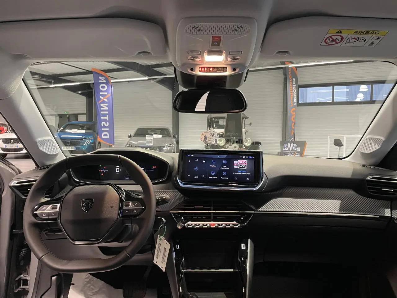 Vue intérieure avant du Peugeot 208 gris Selenium, tableau de bord avec écran tactile et volant compact cuir noir.