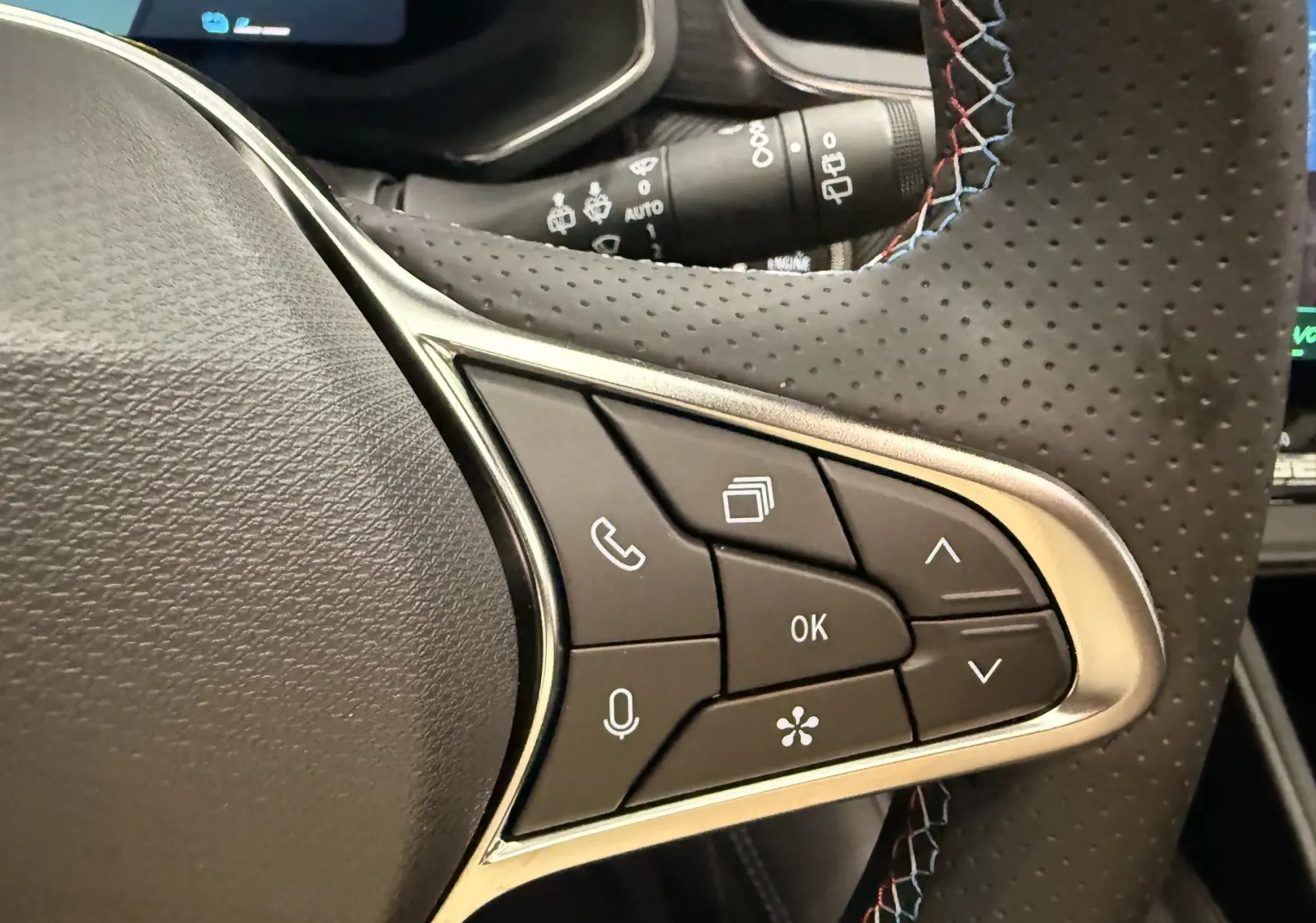 Gros plan sur le volant en cuir perforé avec surpiqûres tricolores du Renault Symbioz gris, boutons de commande multifonctions visibles.