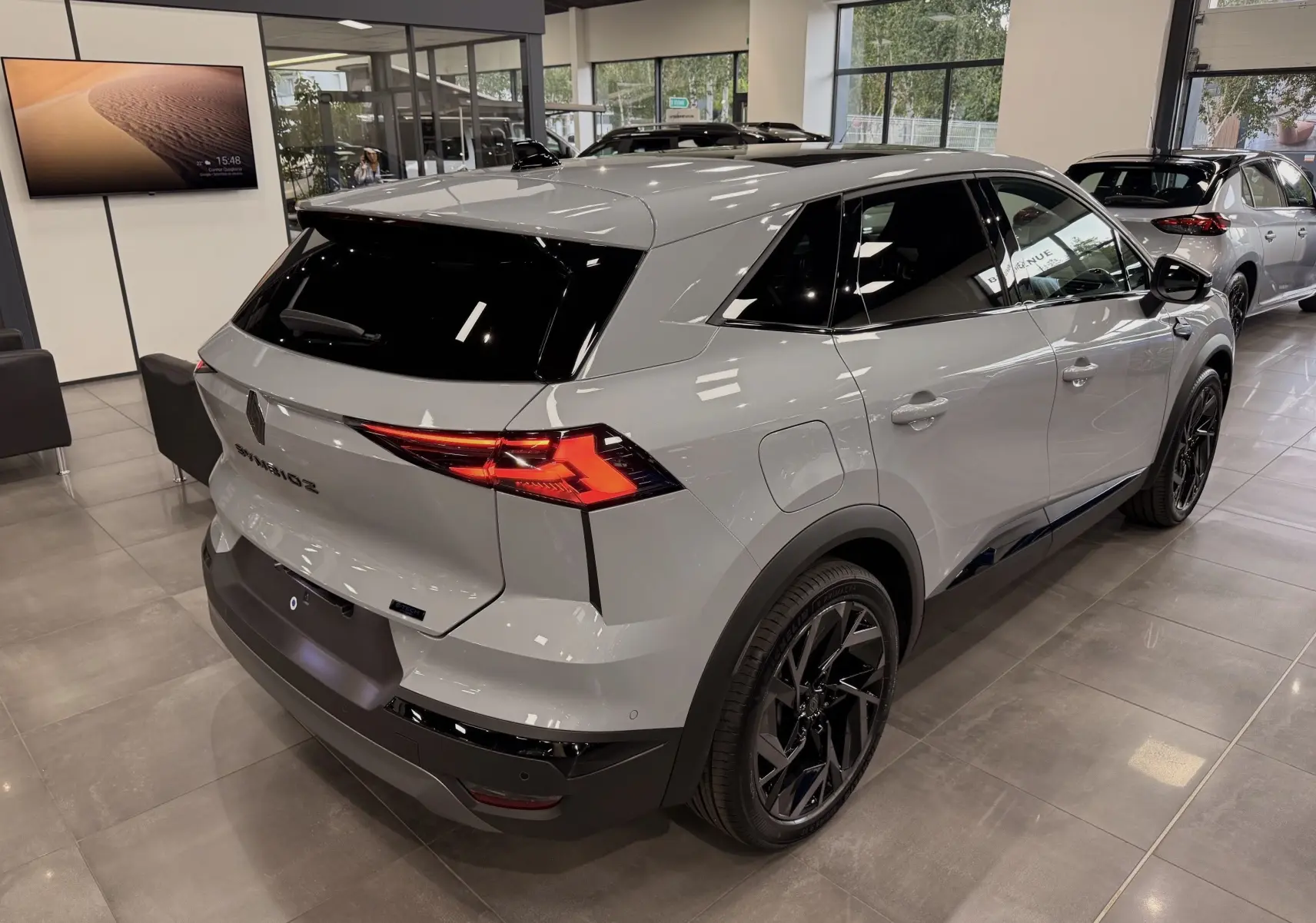 Vue 3/4 arrière droite du Renault SYMBIOZ gris Rafale en showroom, avec feux arrière LED et jantes noires distinctives.