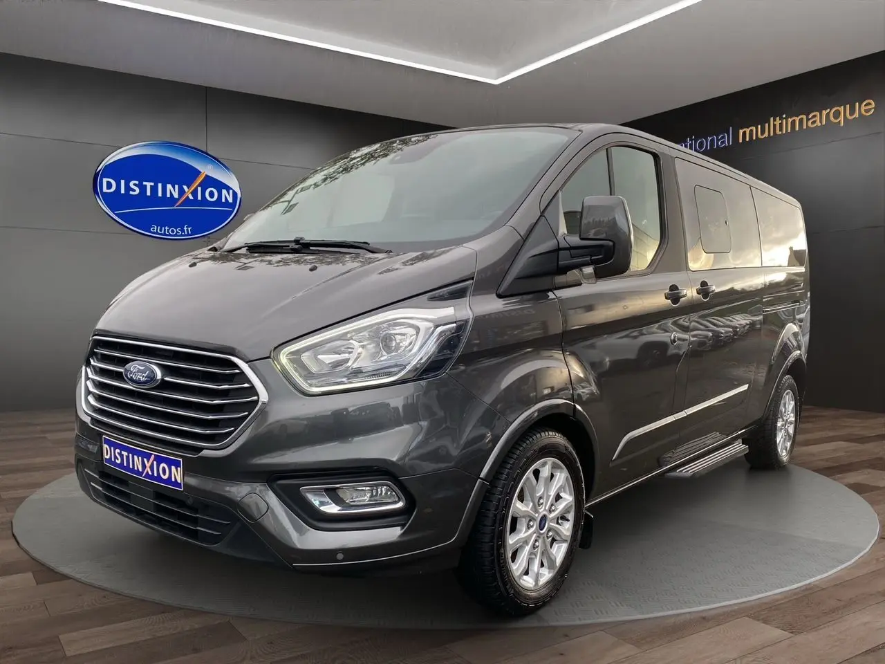 Ford Tourneo Custom gris magnetic vu en 3/4 avant droit, avec jantes alliage et porte latérale coulissante.