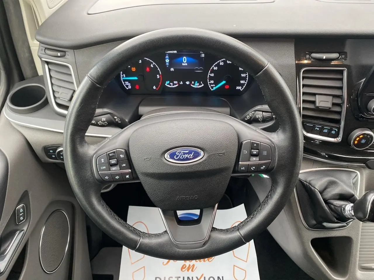 Vue rapprochée du volant noir et du tableau de bord numérique du Ford Tourneo Custom gris Magnetic, avec levier de vitesses manuel.