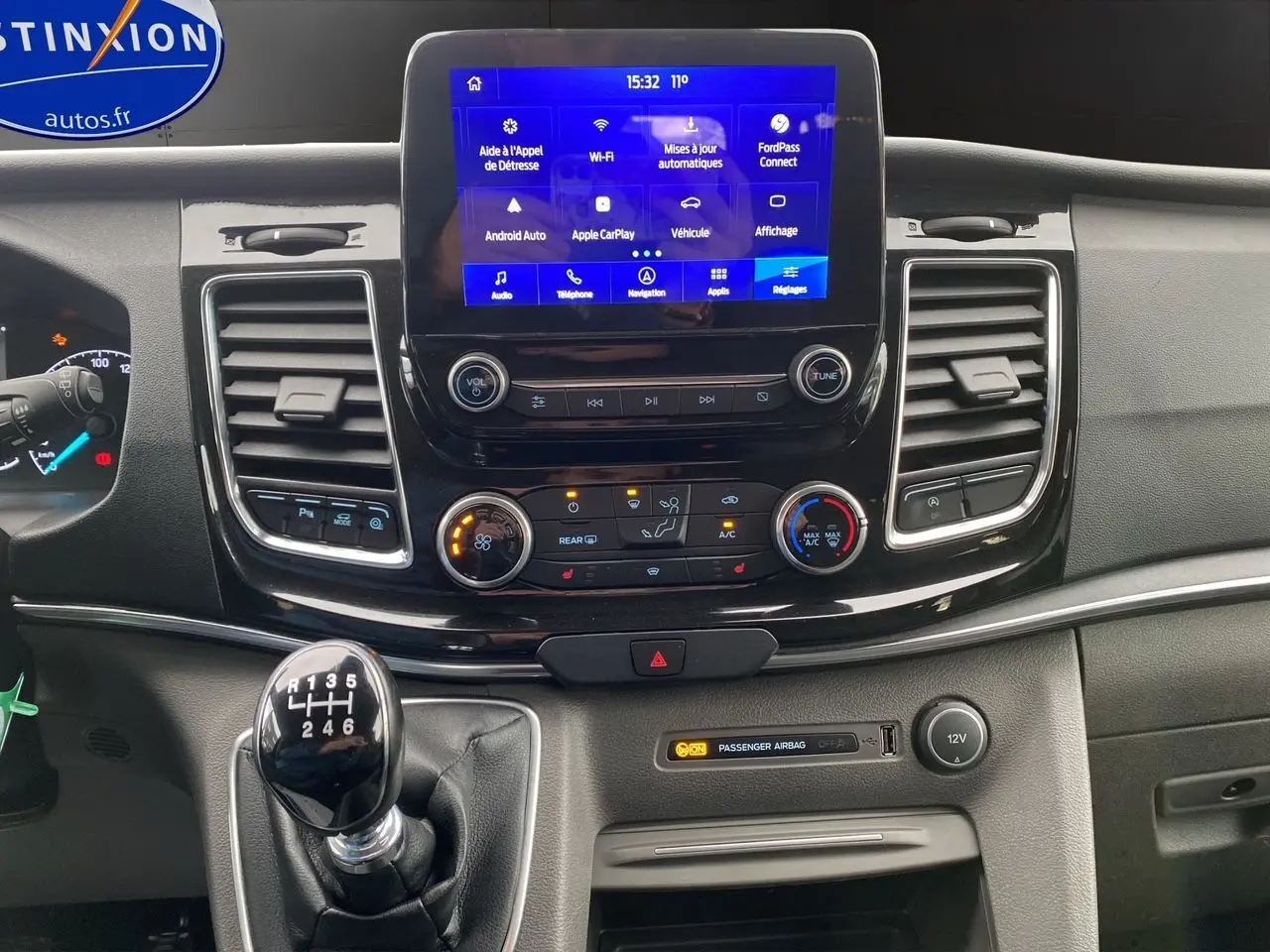 Vue rapprochée du tableau de bord du Ford Tourneo Custom gris, avec écran tactile et levier de vitesses manuel visible.