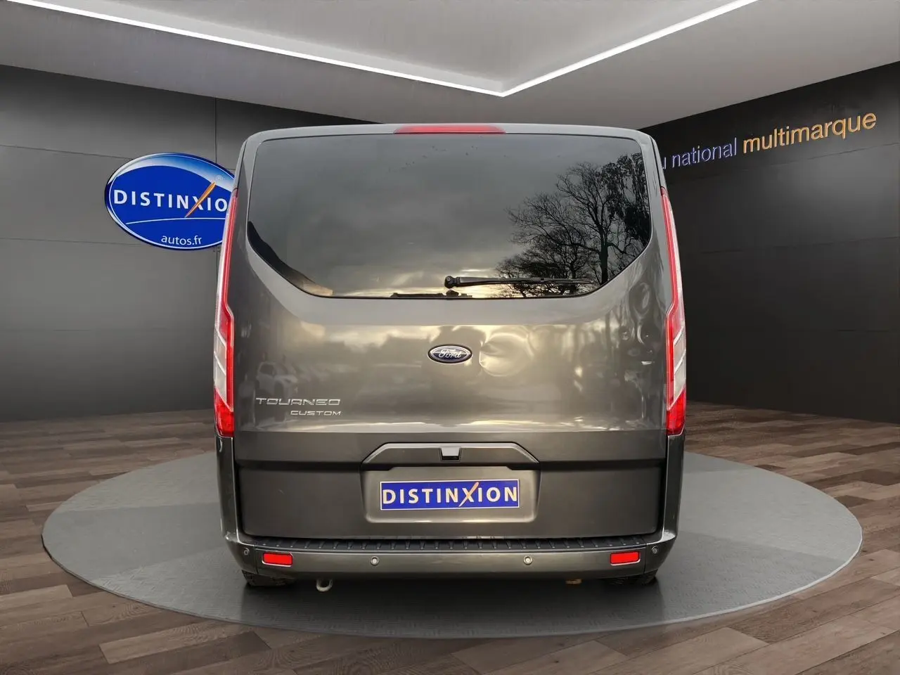 Vue arrière d'un Ford Tourneo Custom gris magnetic avec vitre teintée et feux verticaux rouges.