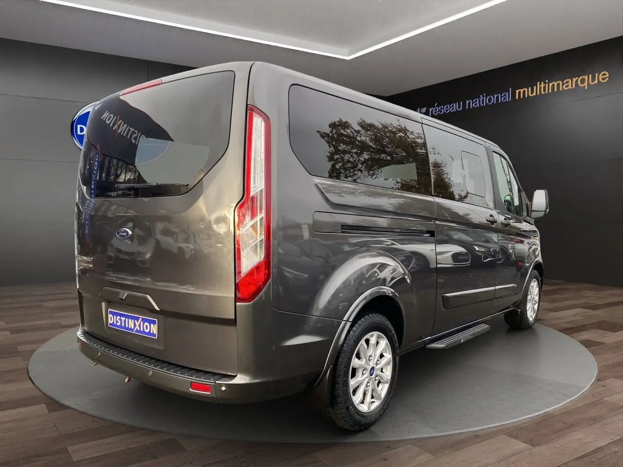 Vue 3/4 arrière droite d'un Ford Tourneo Custom gris magnetic avec vitres teintées et jantes alliage.