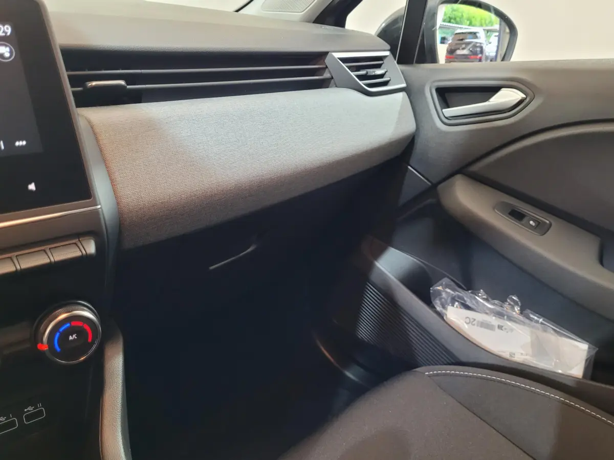 Vue intérieure côté passager de la Renault Clio gris foncé 2025, avec tableau de bord textile et commandes climatisation visibles.