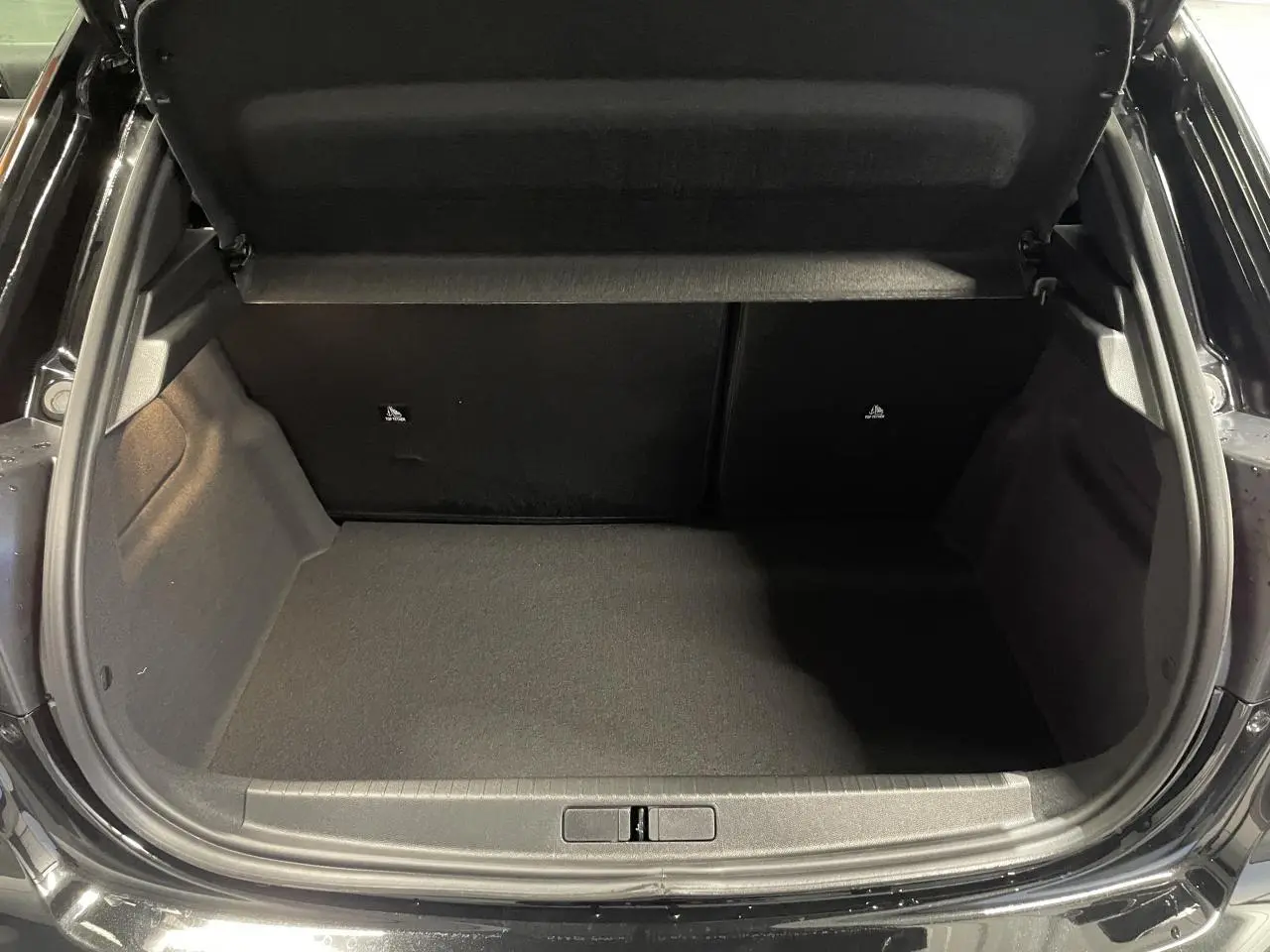 Coffre ouvert vu de l'arrière d'une Peugeot 208 noire métallisée, espace de chargement vide et propre.