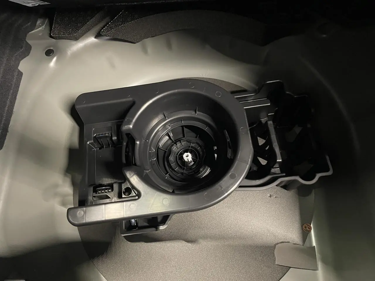 Gros plan sur le rangement de roue de secours dans le coffre d'une Peugeot 208 noire métallisée, sans roue visible.