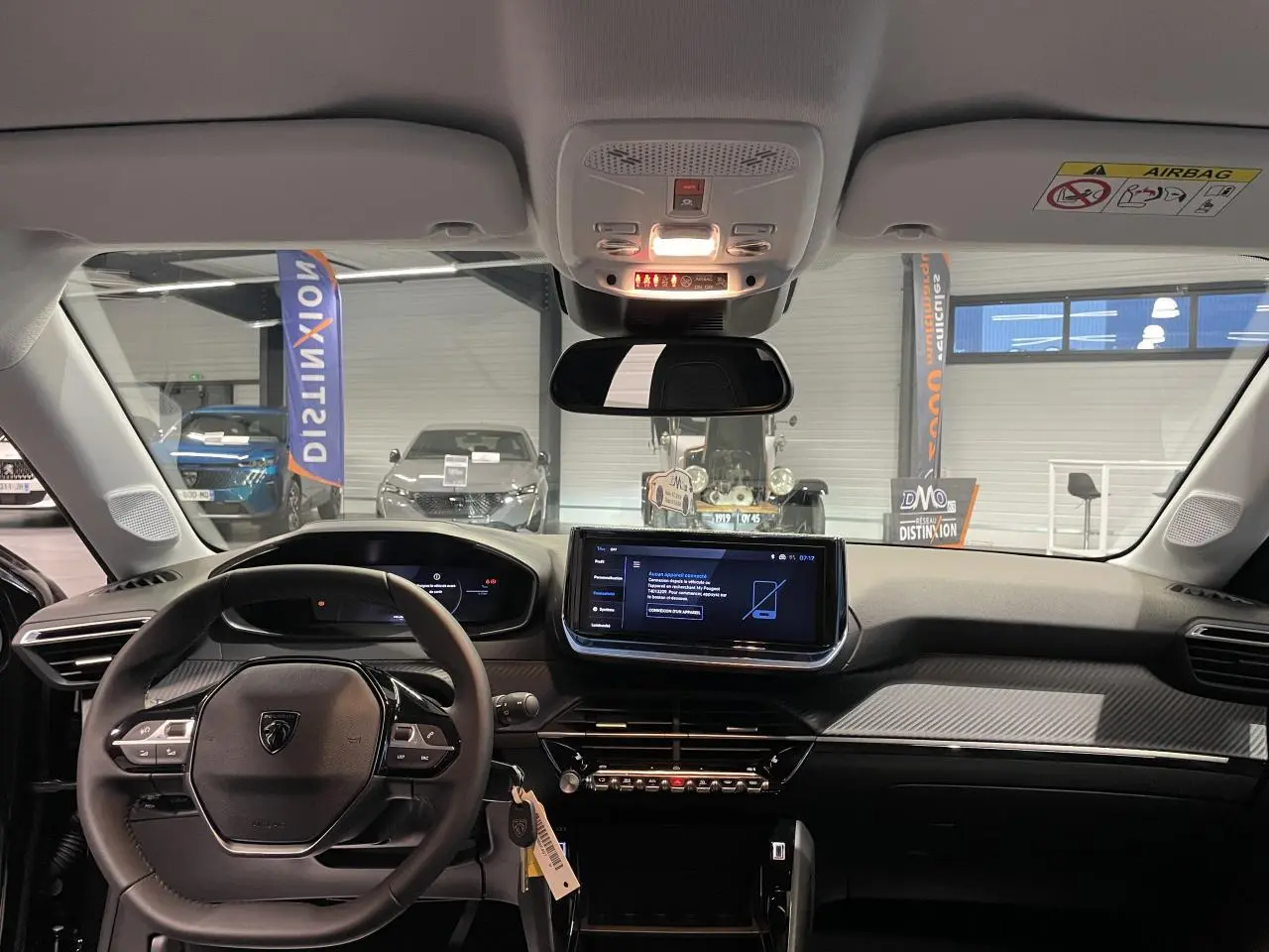 Vue intérieure avant du tableau de bord de la Peugeot 208 noire métallisée avec écran tactile central et volant compact cuir.