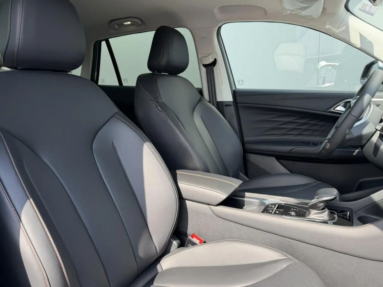 Vue intérieure côté droit du MG MOTOR EHS 1.5 Hybrid+ 224 Luxury 2026 avec sellerie simili cuir noir et accoudoir central.