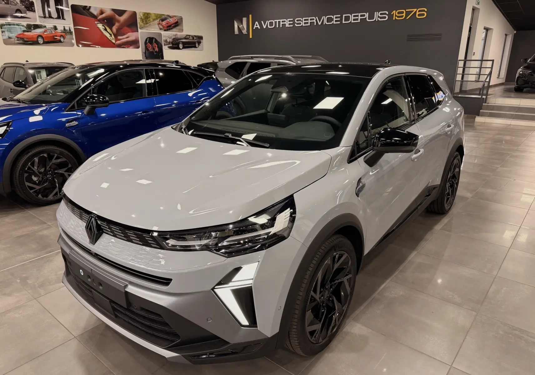 Renault Symbioz gris Rafale en 3/4 avant droit dans un showroom, avec jantes noires et éclairage LED distinctif.