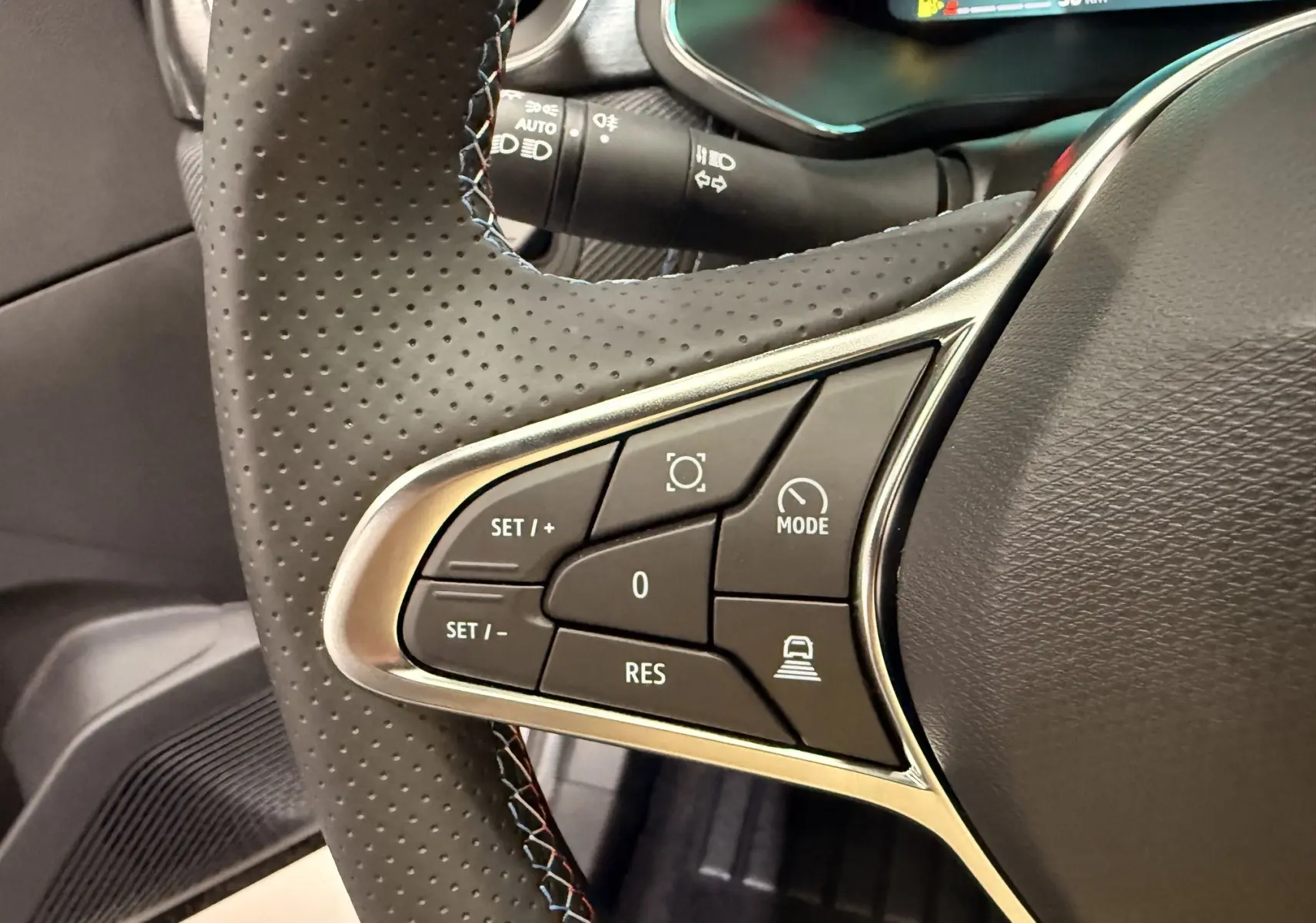 Gros plan sur les commandes gauche du volant perforé noir du Renault SYMBIOZ gris Rafale, avec boutons de régulateur et mode conduite.