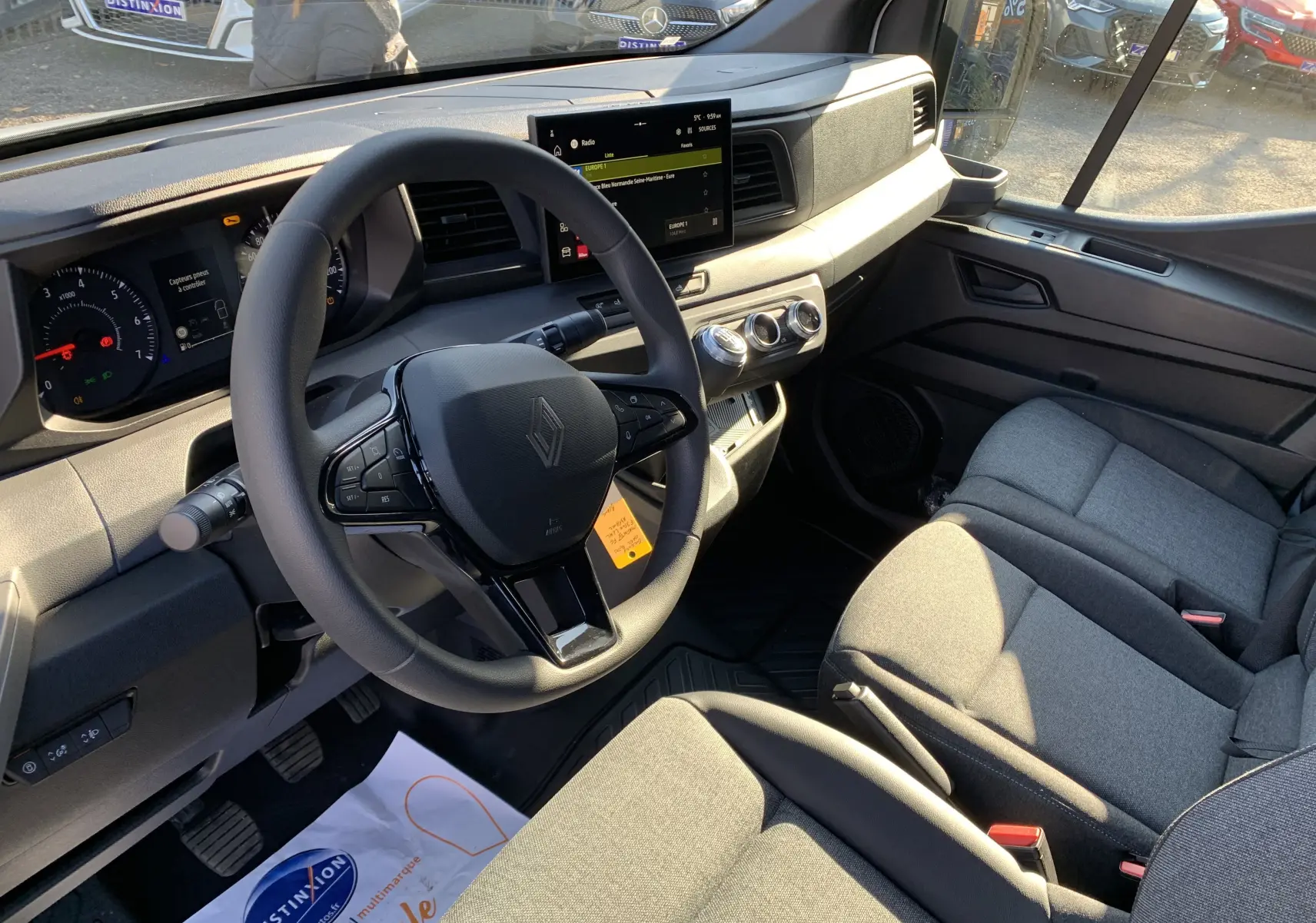 Intérieur du Renault Master 2025 vu côté conducteur, volant multifonction et sièges tissu gris sous lumière naturelle.