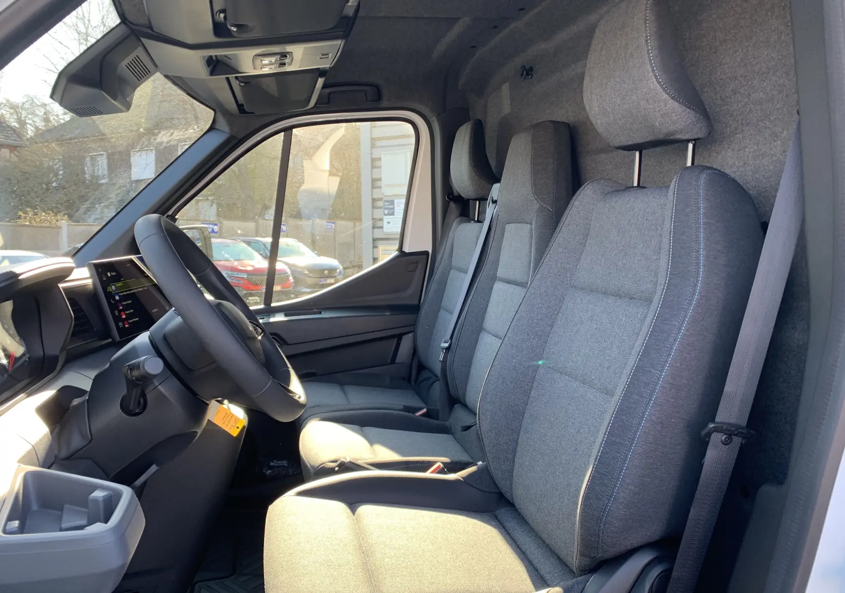 Vue intérieure côté conducteur du Renault Master 2025 blanc mine, sièges tissu gris avec surpiqûres bleues.