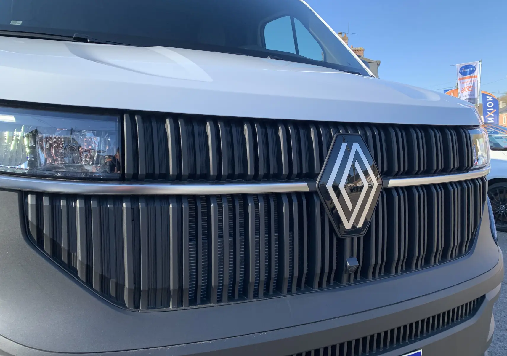 Gros plan sur la calandre noire et le logo Renault d’un Renault Master blanc mine, vue de face par temps clair.