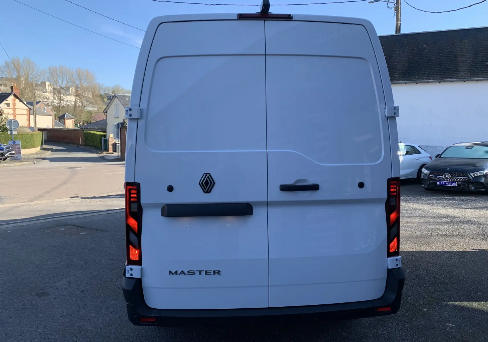 Vue arrière d'un utilitaire Renault Master blanc mine avec feux arrière allumés et logo central visible.