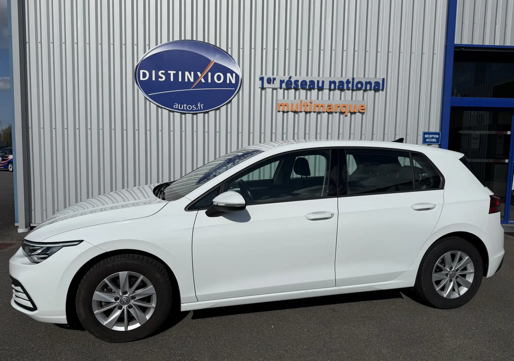 Profil droit d'une Volkswagen Golf blanche 1.0 TSI 110 Life de 2020, garée devant un mur avec logo Distinxion.