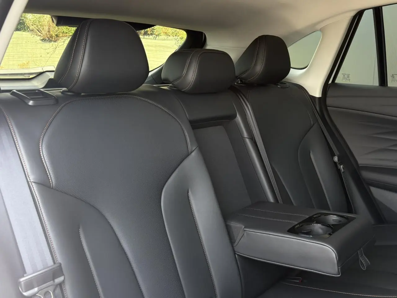 Vue intérieure des sièges arrière noirs en simili cuir avec accoudoir central et porte-gobelets du MG Motor EHS blanc.