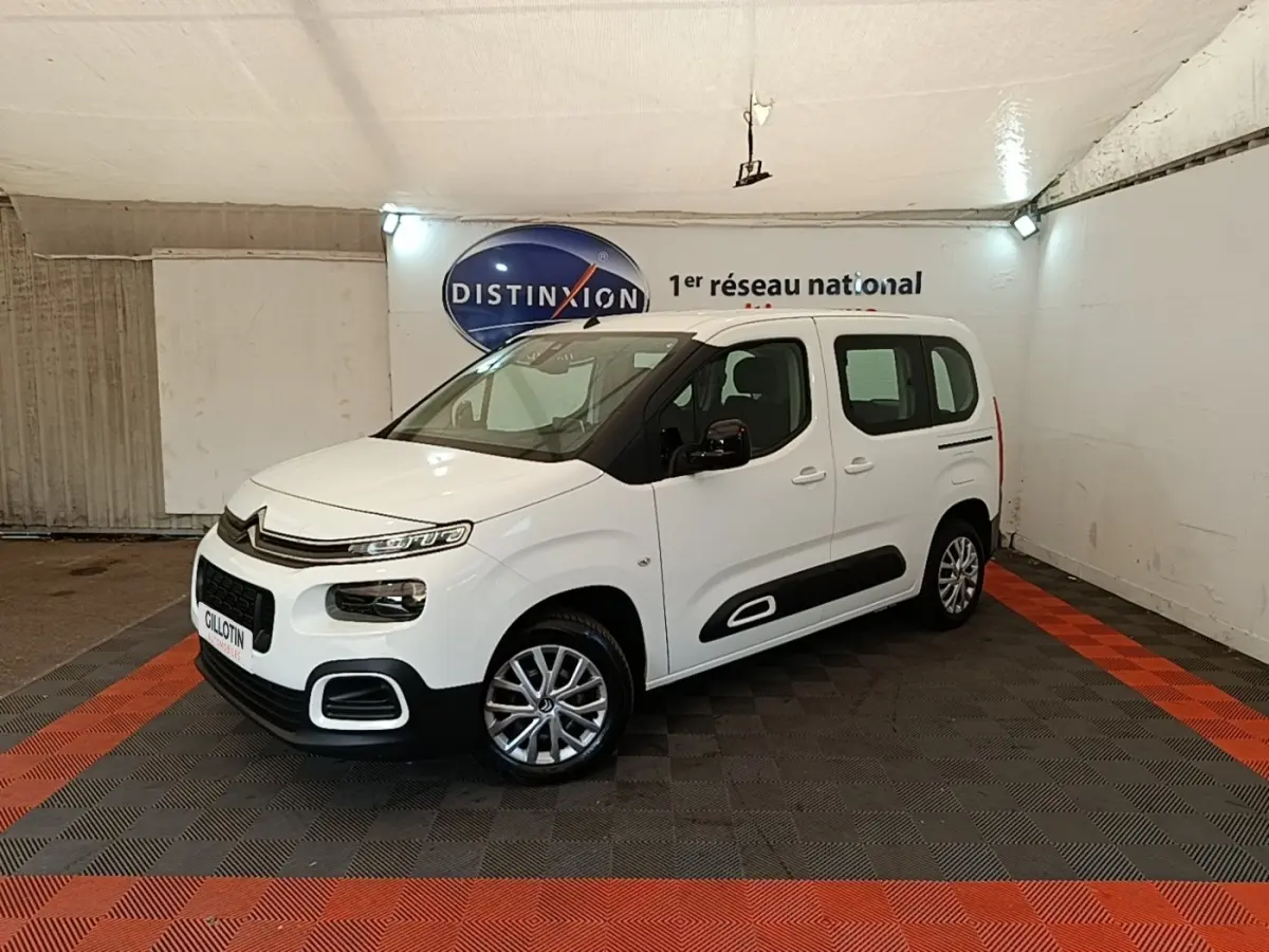 Vue 3/4 avant droite du Citroën Berlingo blanc avec protections latérales noires et jantes alliage en intérieur showroom.