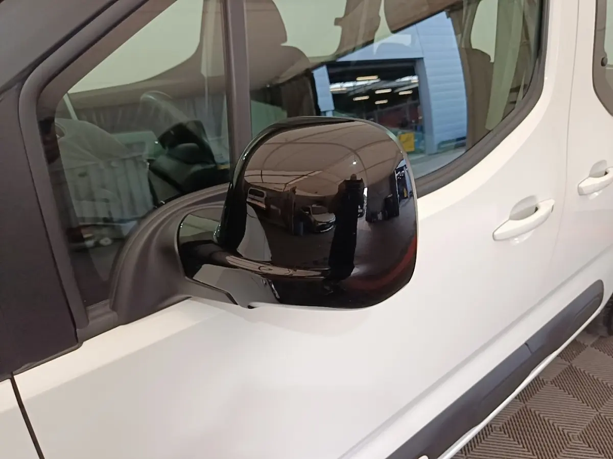 Rétroviseur noir en gros plan sur le côté gauche d’un Citroën Berlingo blanc, vue partielle latérale.