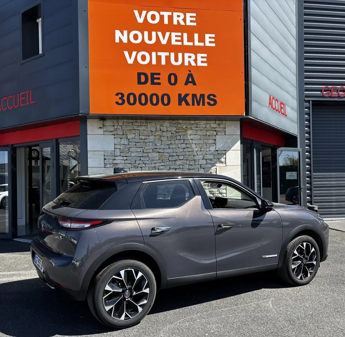 Vue 3/4 arrière droite d'une DS3 1.2 PureTech 130 Auto Esprit de Voyage gris foncé avec jantes noires et toit noir.
