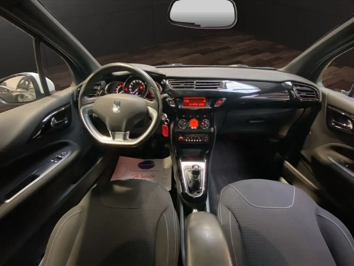 Vue intérieure avant de la Citroën DS3 e-HDi 90 Airdream So Chic 2011, tableau de bord noir brillant et volant alu-cuir.