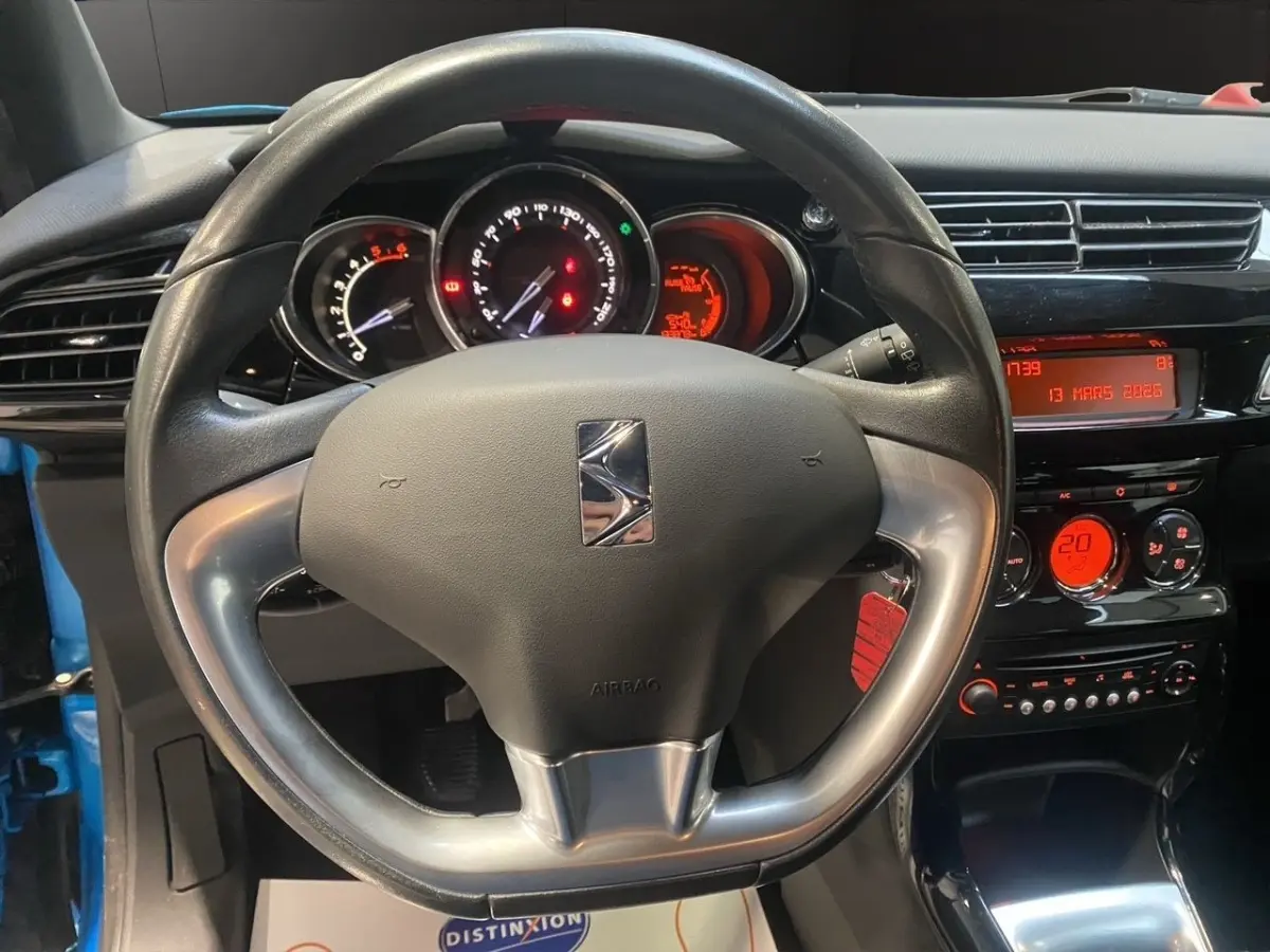 Vue intérieure centrée sur le volant alu et cuir d'une Citroën DS3 bleu, avec tableau de bord et commandes éclairées en rouge.
