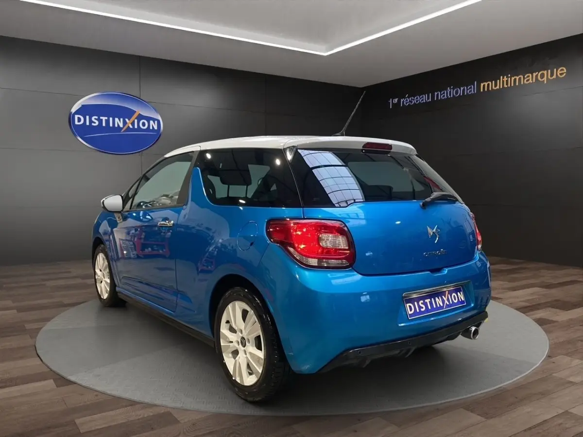 Vue 3/4 arrière droite d'une Citroën DS3 e-HDi 90 Airdream So Chic bleu avec toit blanc et jantes blanches.