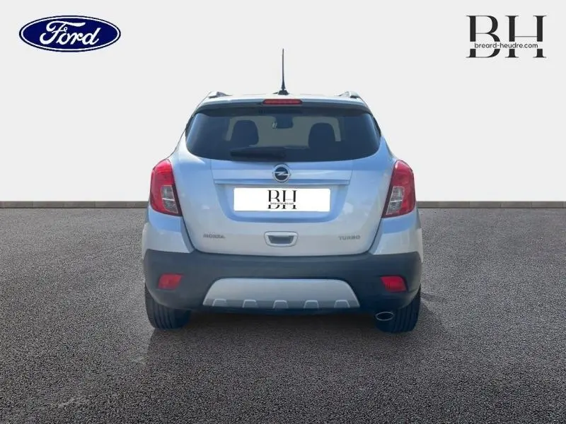 Vue arrière d'un Opel Mokka gris minéral avec feux rouges et pare-chocs noir contrastant sur sol gris.