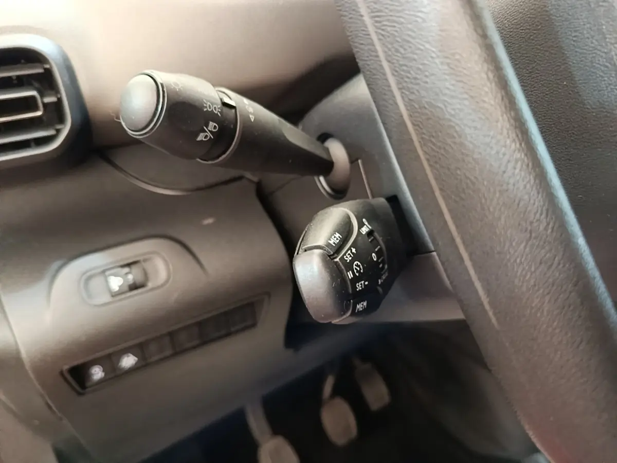 Gros plan sur les commandes au volant côté gauche du Peugeot Rifter blanc, avec boutons de régulateur de vitesse et éclairage.