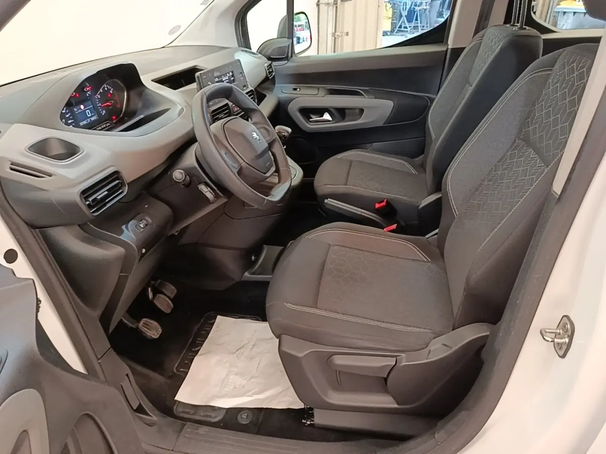 Vue intérieure côté conducteur du Peugeot Rifter blanc 2020, montrant sièges avant gris et tableau de bord avec volant.