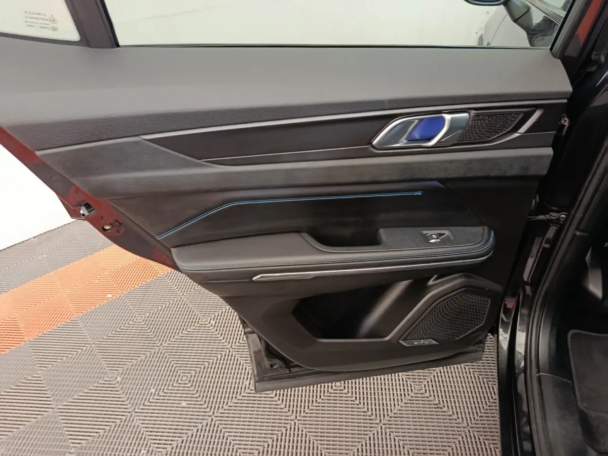 Vue intérieure de la porte arrière droite du LINK & CO 01, garniture noire avec surpiqûres bleues et haut-parleur intégré Bose.